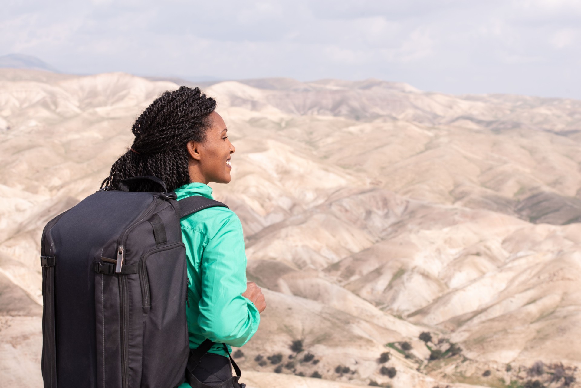 Happy African woman hiking outdoors in desert with bag.